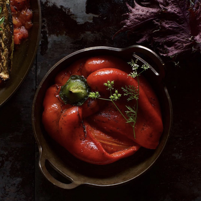 Roasted red bell peppers in a dark carbon steel DARTO Paella with a green herb garnish, presented on a dark rustic table.